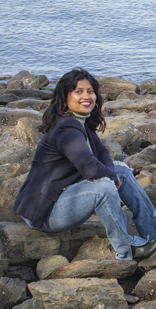 Monica Rao, 2023 Knauss Fellow, sits along rocky shore.