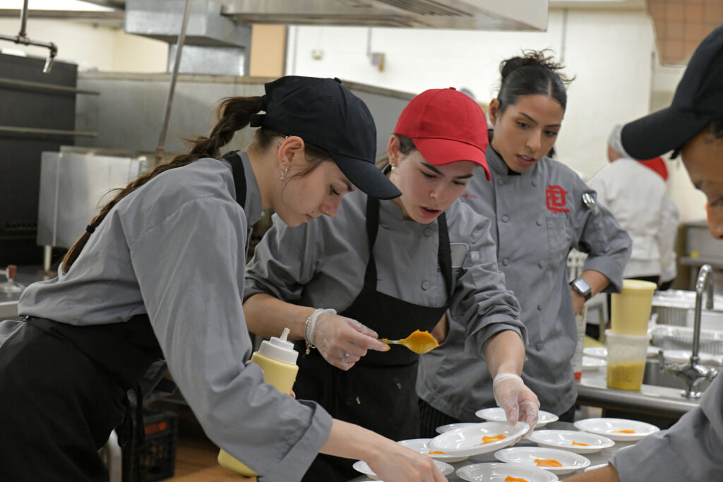 Culinary  students working in the kitchen  working  quickly to plate their flounder recipes.