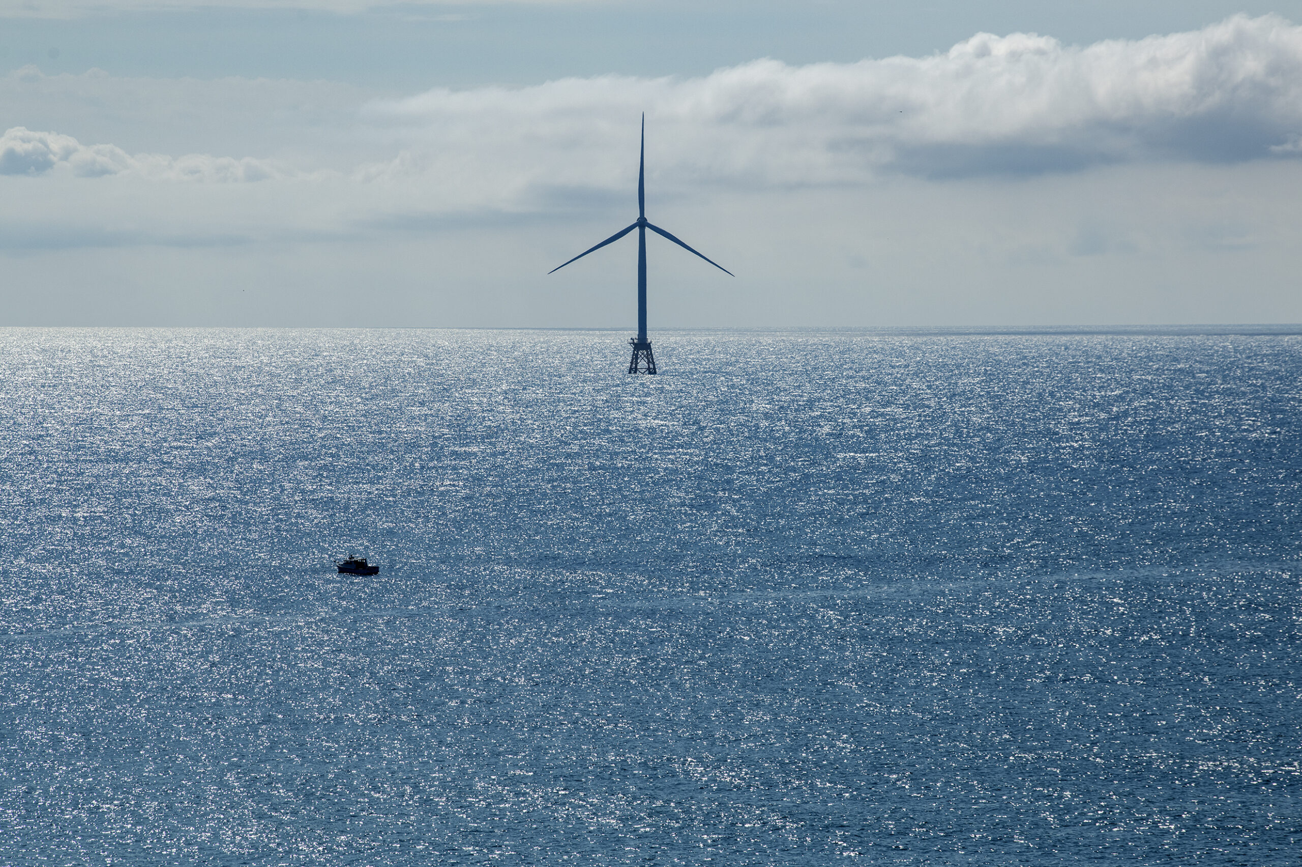A fishing boat passes a turbine in the Block Island offshore wind farm in Rhode Island. Offshore wind companies are creating compensation funds for fishers.