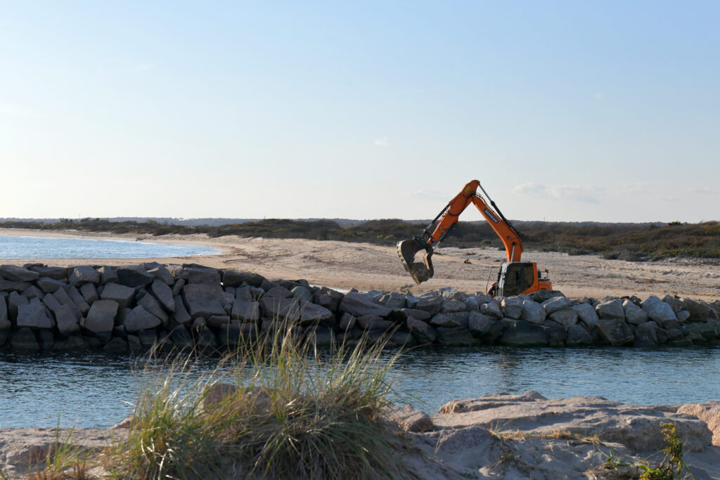 A backhoe places a rock on the Charlestown Breachway west wall