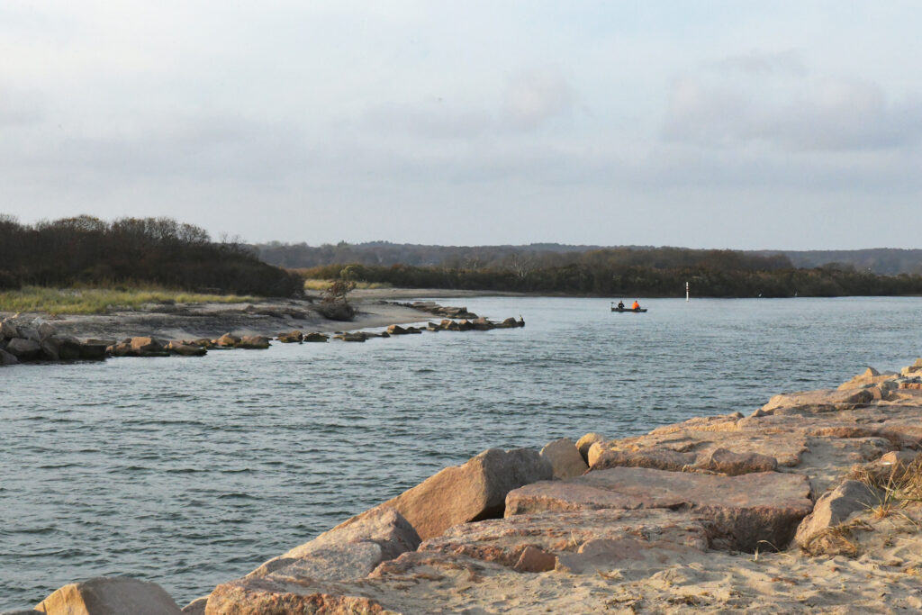 Two people in a small boat approach Elbow Beach, past the rocks of the breachway