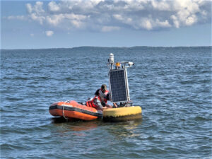 Two people in an infoatable dinghy work on a scientific buoy in Lake Michigan.