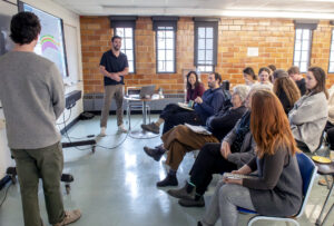 Two students stand in front of a screen as seated audience members look on.