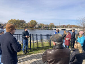 Man in front of fence facing river talks to group