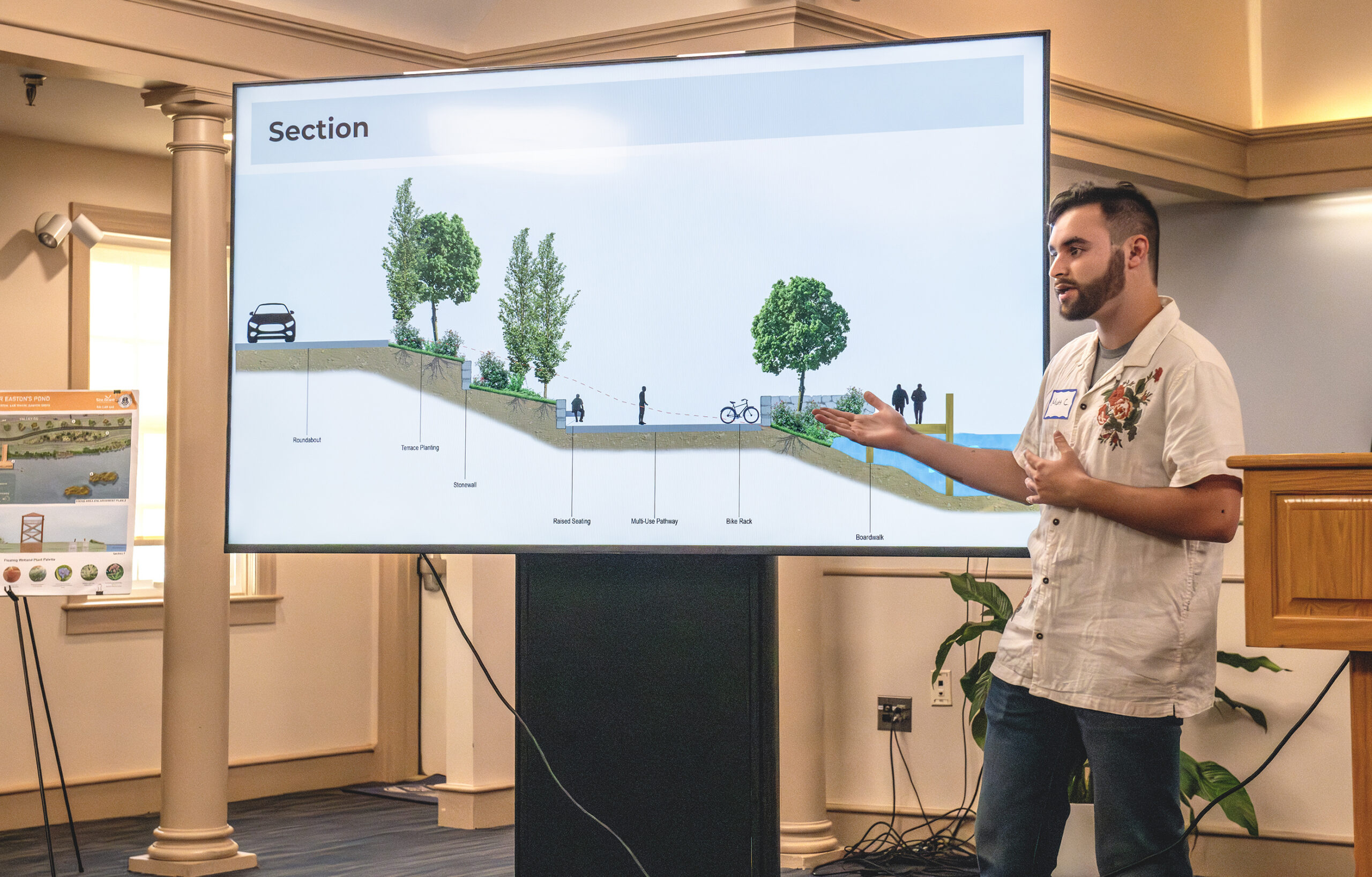 A student gestures in front of a screen with a slide showing a cross section of a streetscape