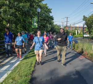 A group of people walks along a bike path surrounded by trees and plants