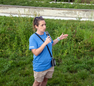 A person speaks into a microphone at a grassy park area