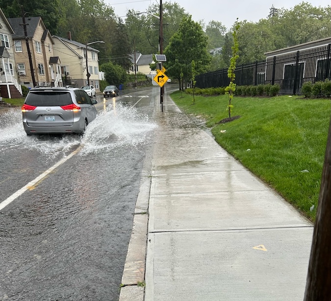 Cars drive through flooded residential road.